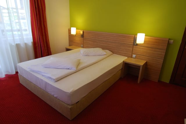 Dormitor cu perete verde — pat matrimonial, veioze și lumină naturală